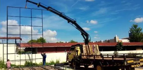 Truck-mounted crane lifting a steel grid frame beside a building
