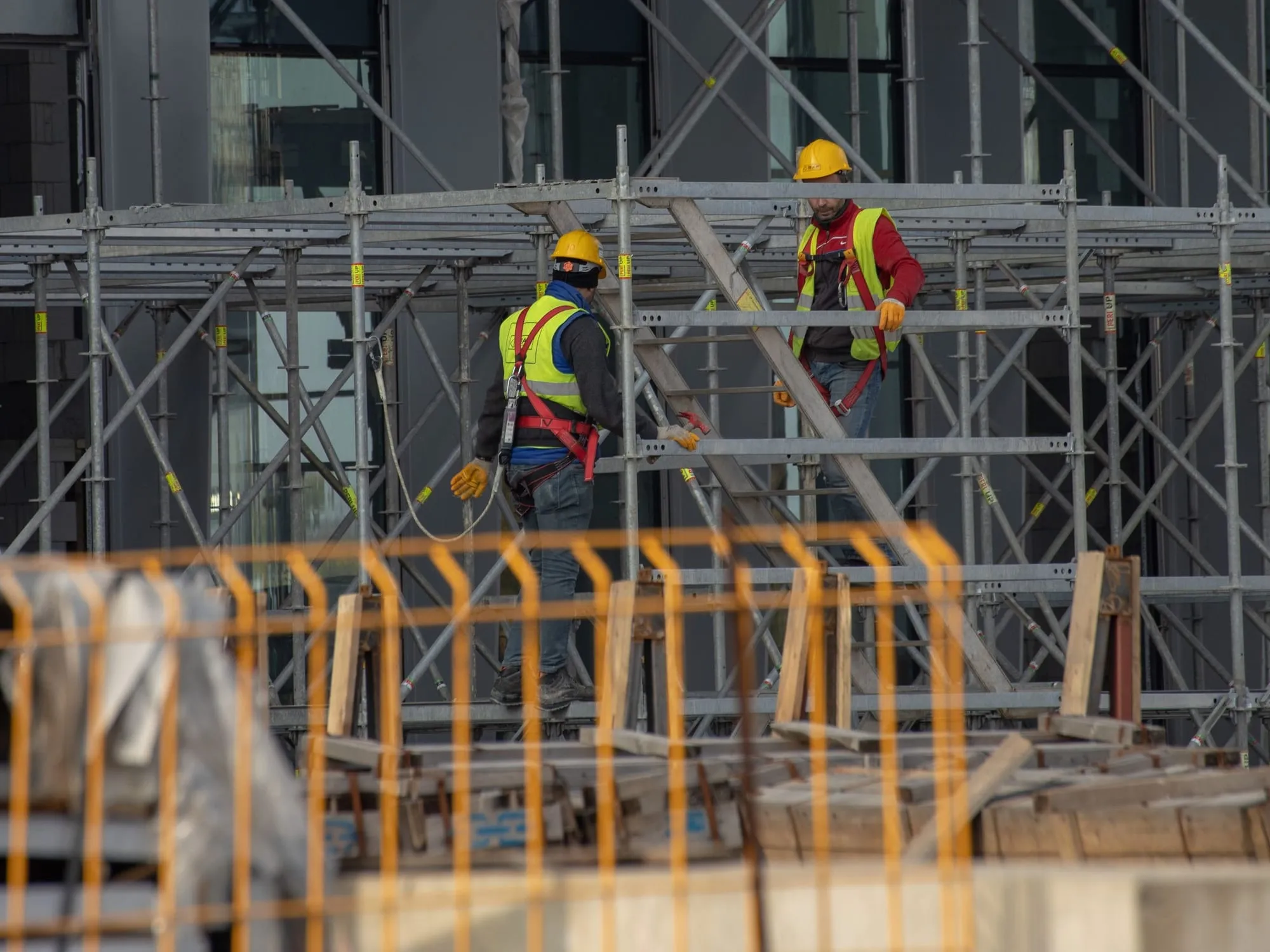 Pekerja konstruksi dengan helm, rompi, dan full body harness di perancah